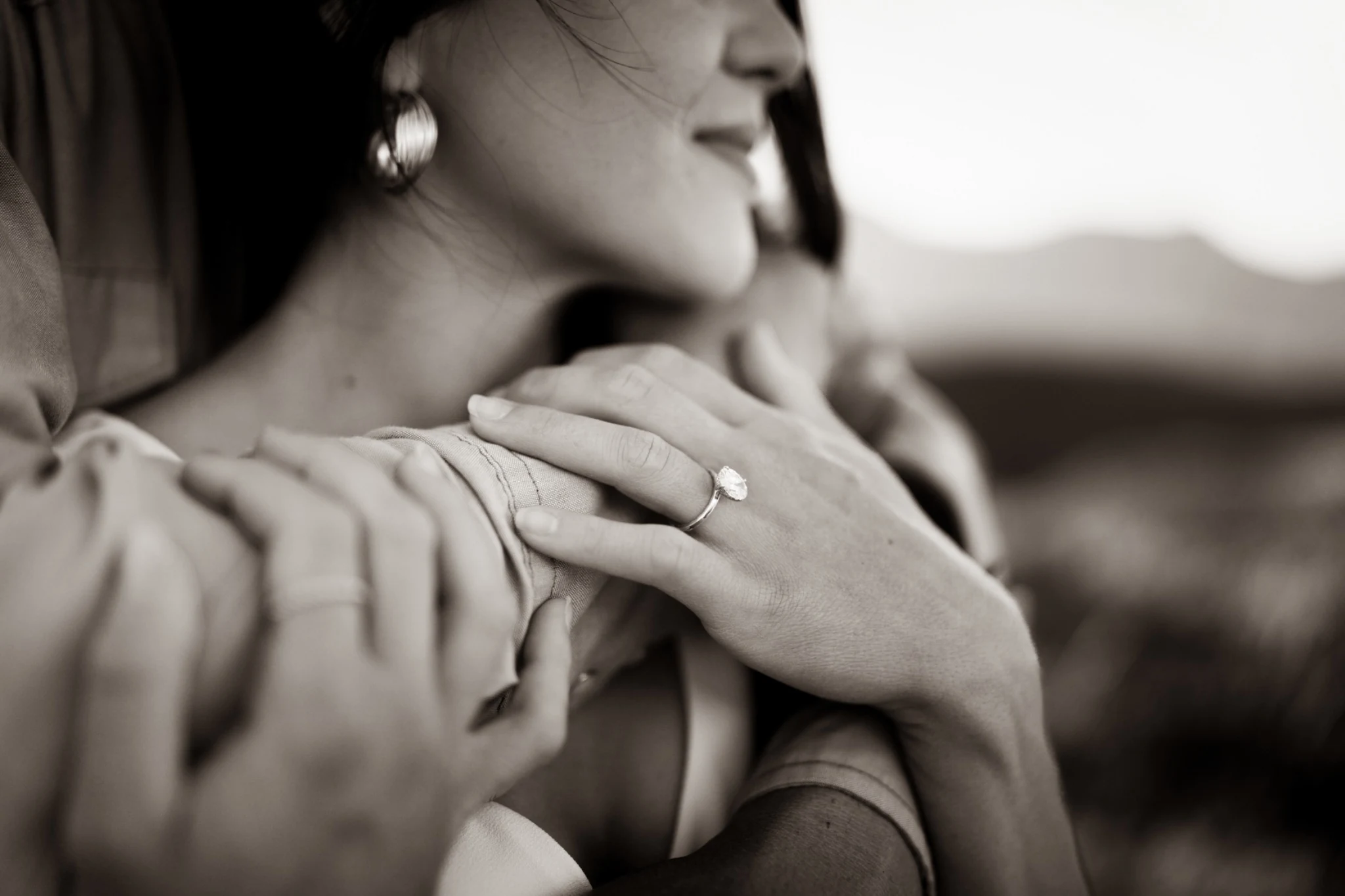 Black-and-white close-up of an engagement ring and intertwined hands