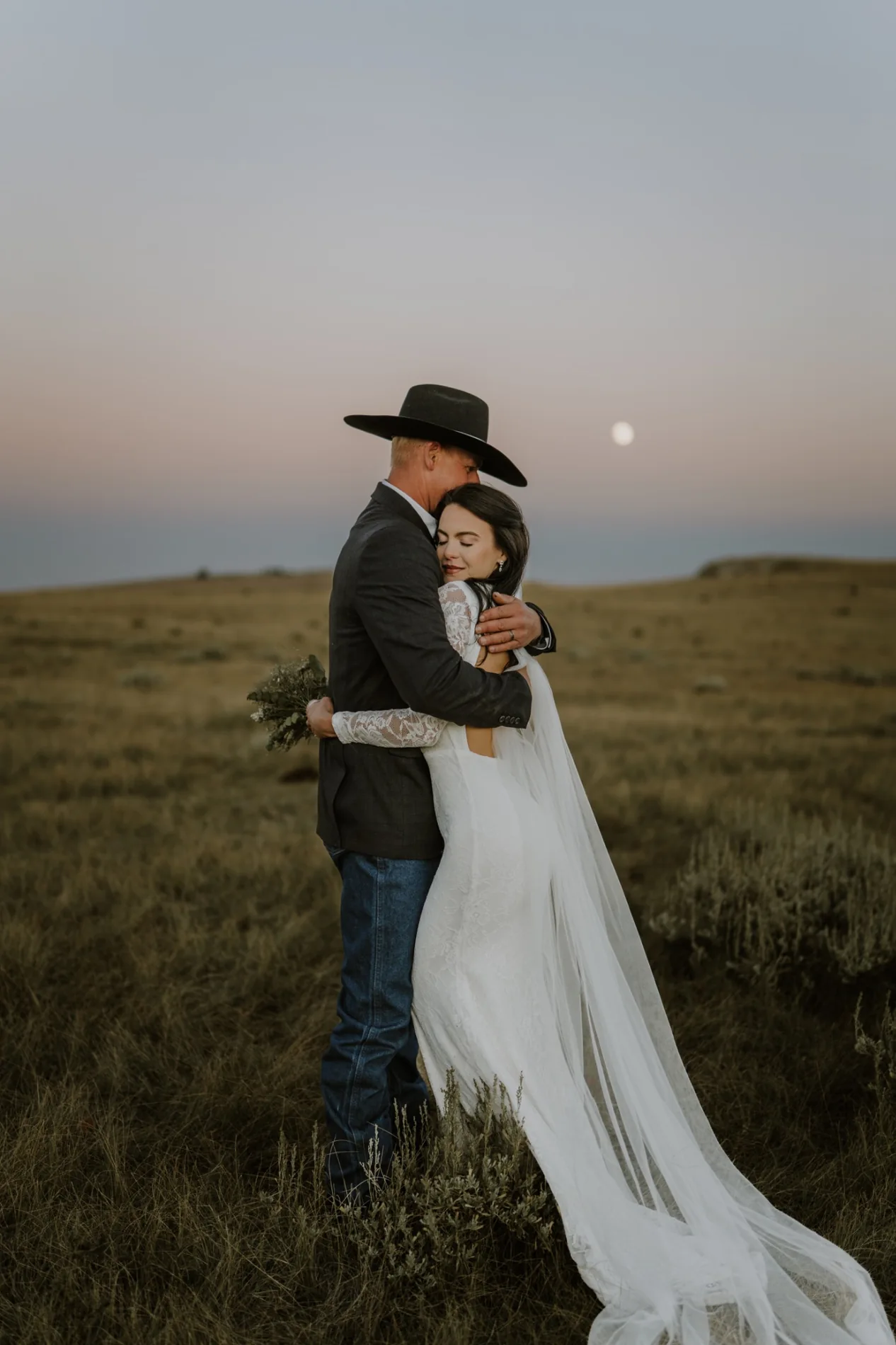 Bride and groom holding one another at dusk in a Wyoming meadow